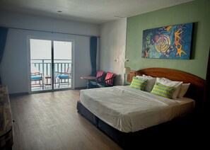 A hotel room with a bed, a balcony with chairs, and a painting on the wall. - Sugar and Spice Inn (Karon)