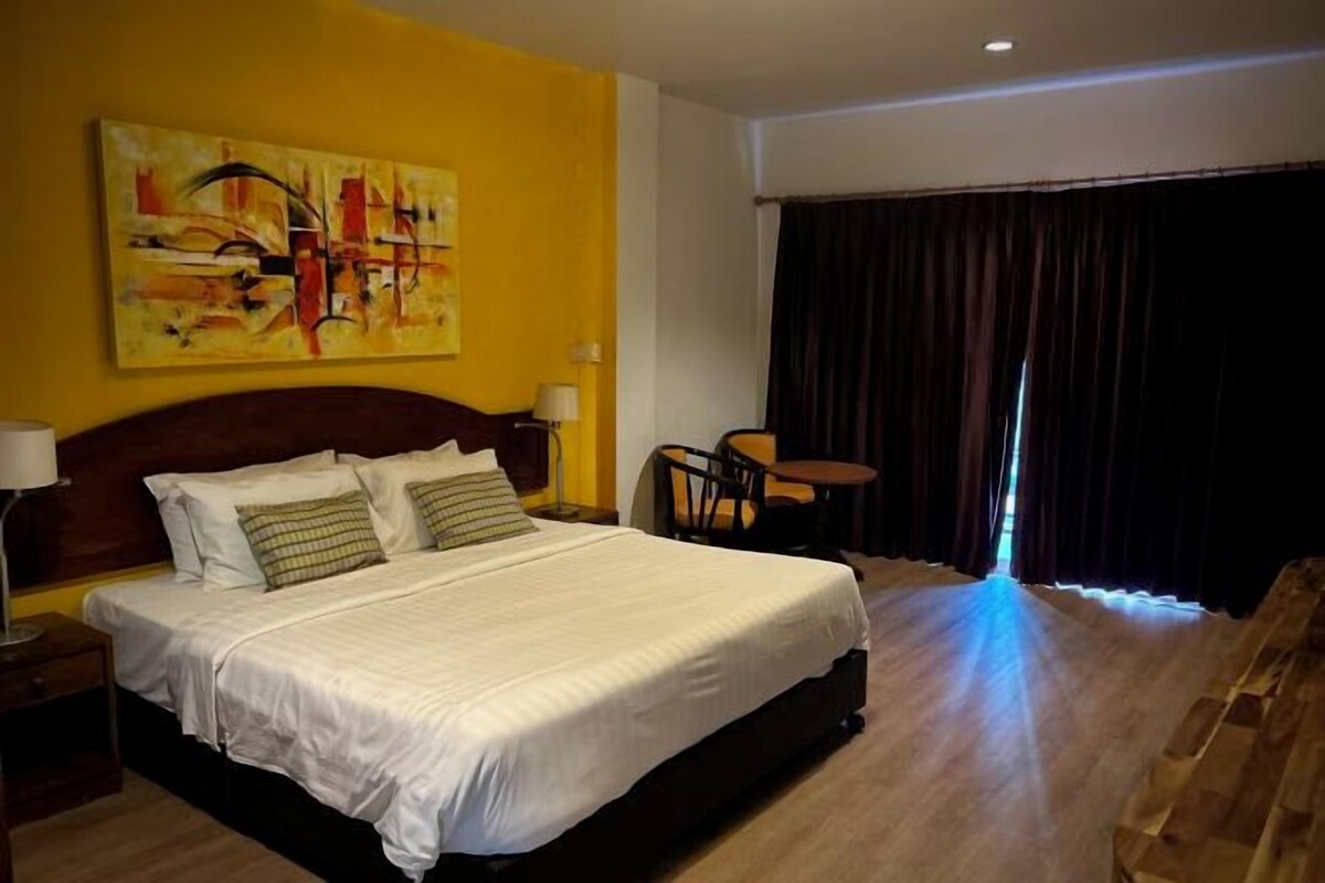 A hotel room with a large bed, a desk, a chair, a painting on the wall, and a view of the outside.