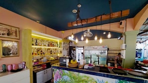 A bar area with a counter, shelves with bottles, and a mural on the wall. - Sugar and Spice Inn (Karon)