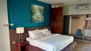 A neatly arranged hotel room with a bed, bedside table, lamp, and a painting on the wall. - Sugar and Spice Inn (Karon)