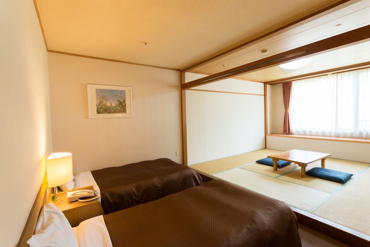 A hotel room with two beds, a small table, a lamp, and a painting on the wall.