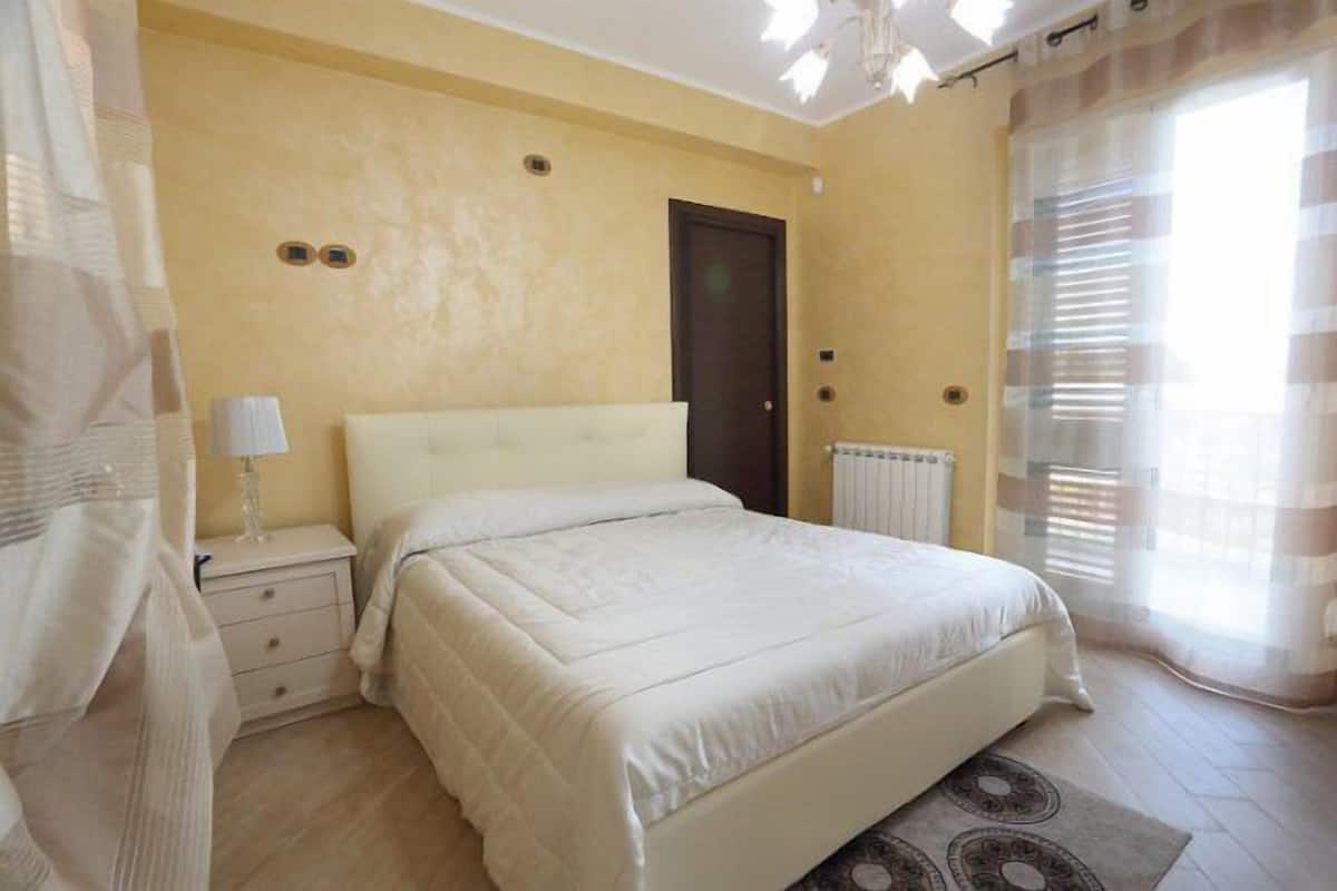 Un dormitorio con cama, mesita de noche y cortinas.