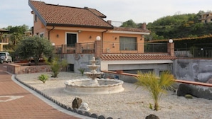 Ein zweistöckiges Haus mit einem Ziegeldach, einem kleinen Garten mit Brunnen und einer gepflasterten Auffahrt.