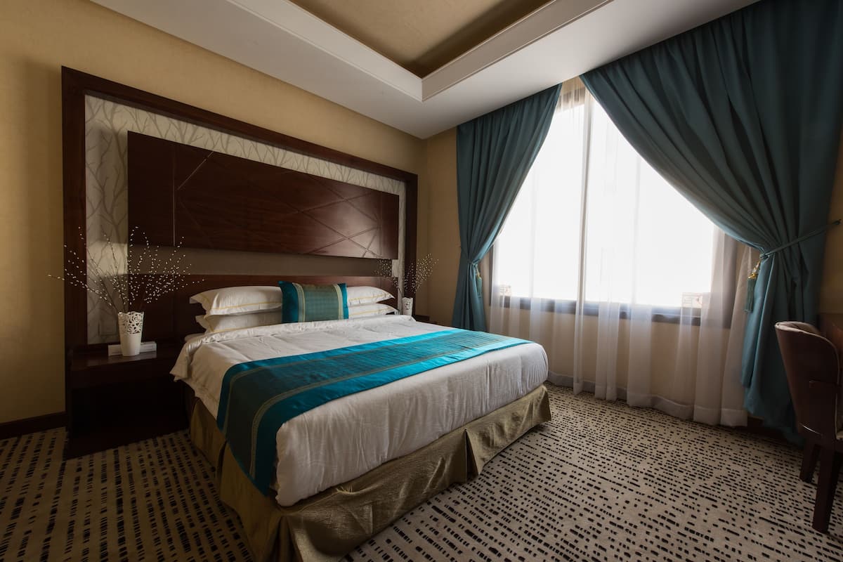 Una habitación de hotel con una cama grande, cabecera con diseño geométrico, ventana con cortinas y alfombra estampada.