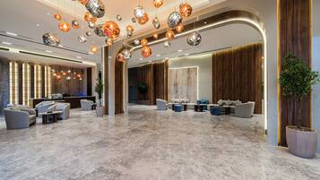 A spacious lobby with a marble floor, modern seating, and a variety of hanging spherical light fixtures.