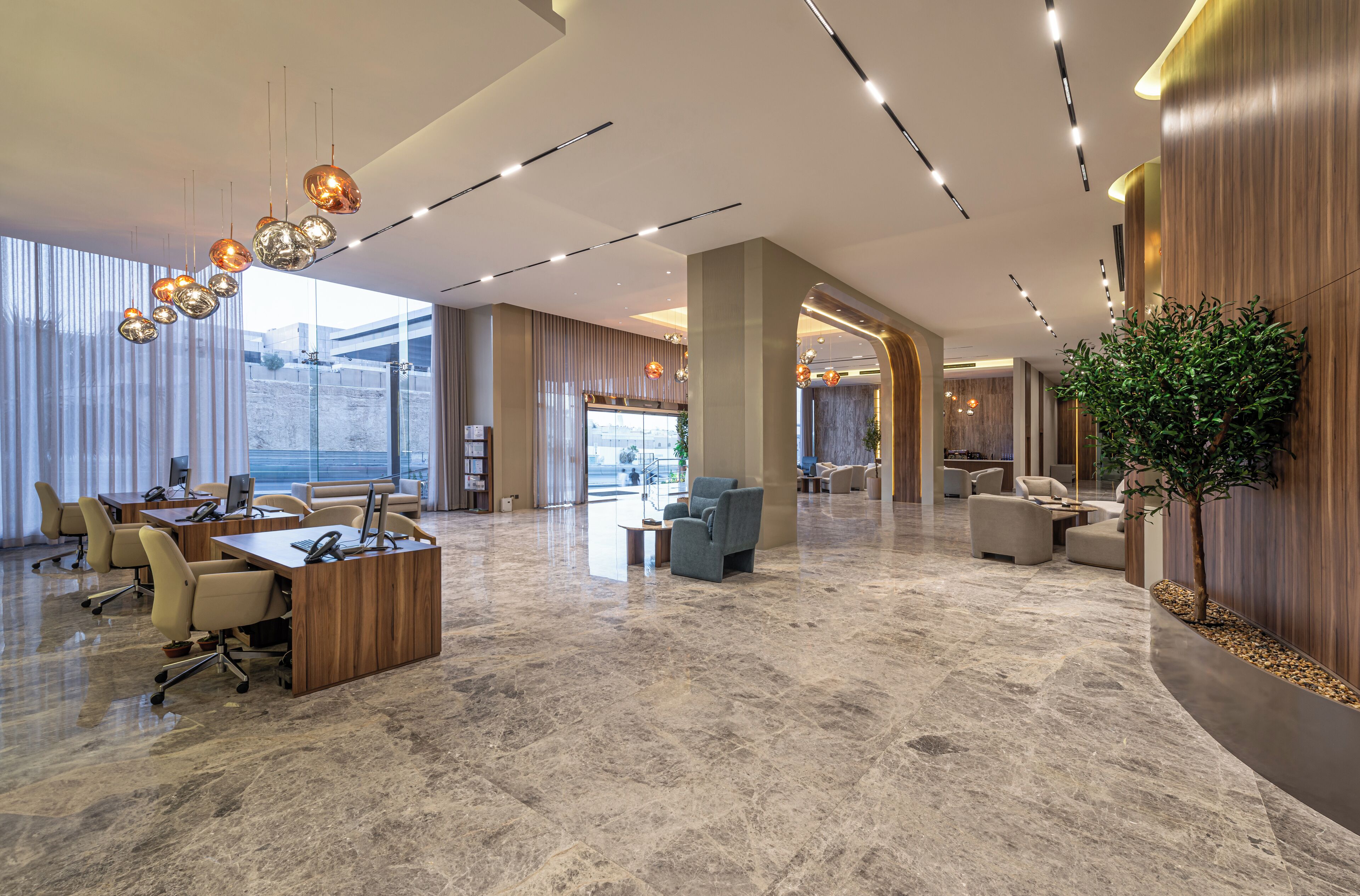 A spacious lobby with a marble floor, modern furniture, and a large plant.