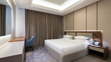 A modern hotel room with a large bed, a desk, a chair, and a nightstand with a phone.