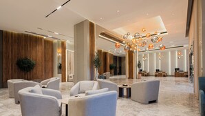 Un vestíbulo amplio con mobiliario moderno, un candelabro y piso de mármol.