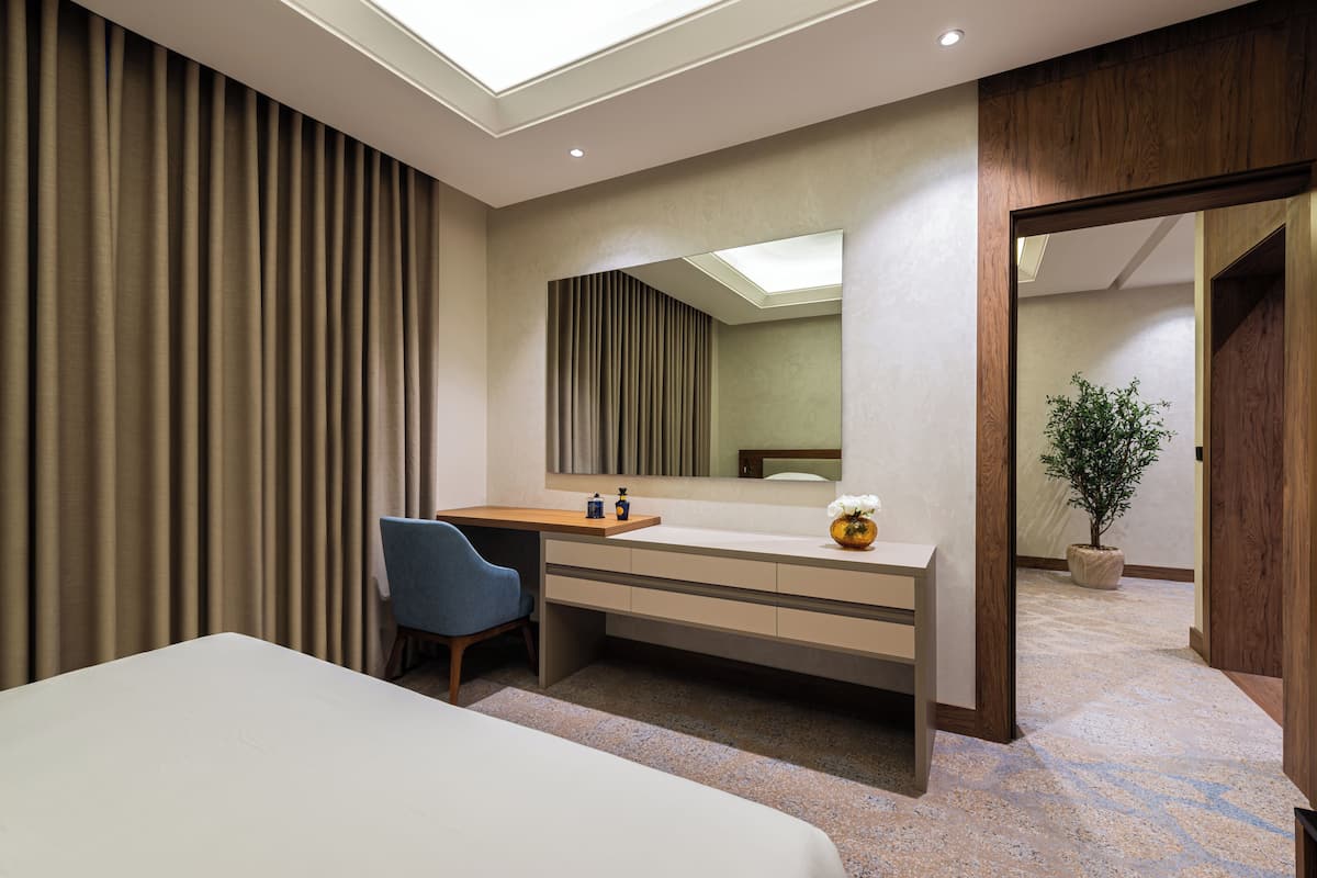 Una habitación de hotel moderna con cama, escritorio, silla, un espejo grande y una planta en maceta.