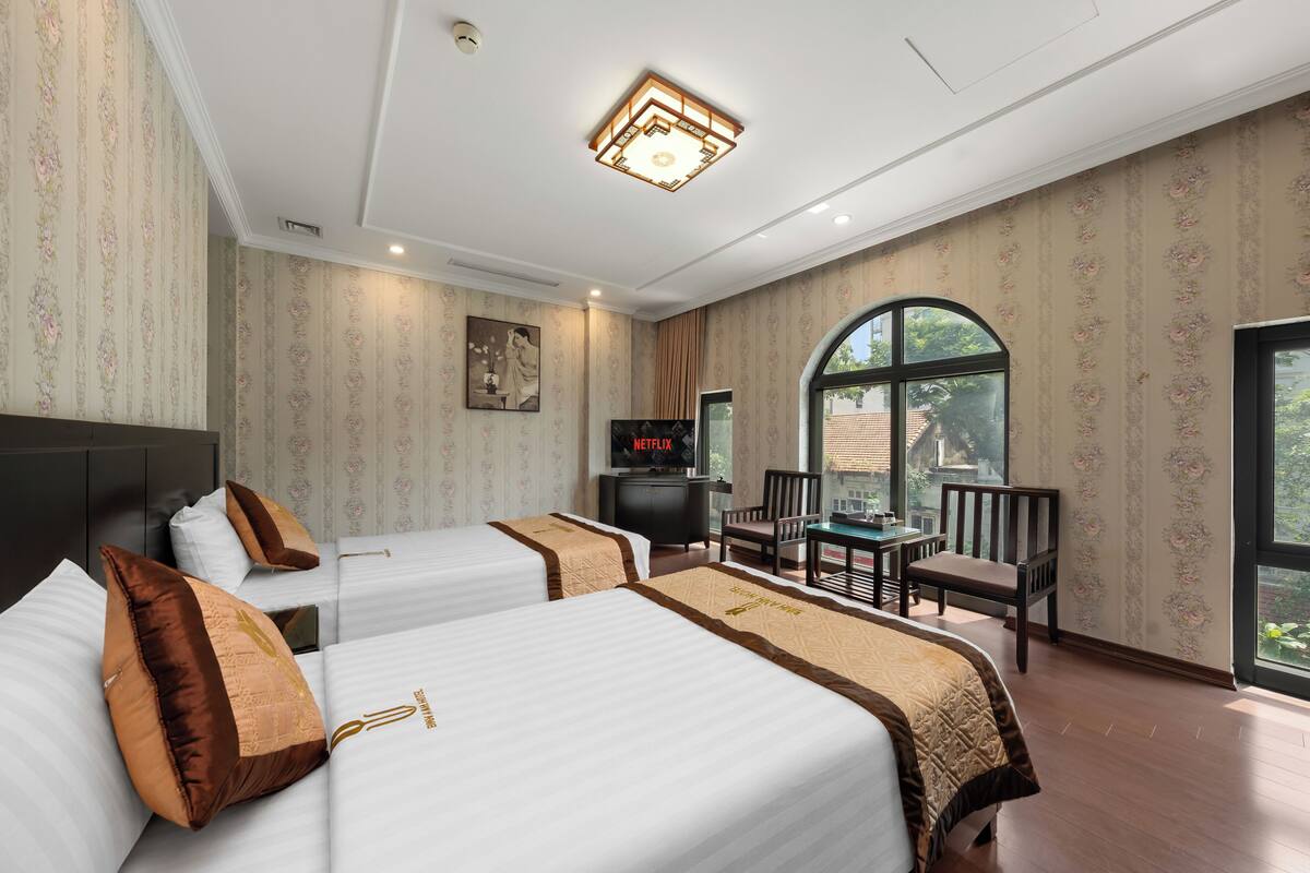 A hotel room with two beds, a television, a desk, and a large window.