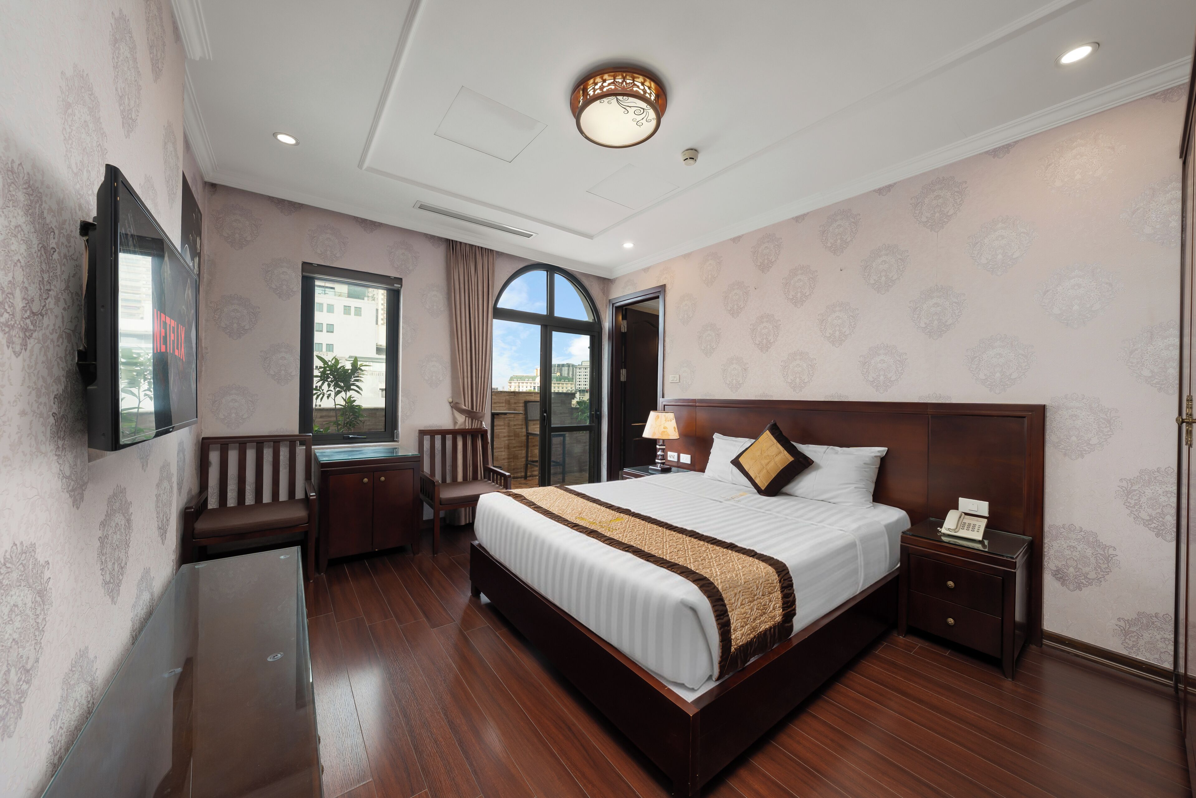 A hotel room with a large bed, a desk, a chair, a TV, and a window with curtains.