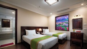 Une chambre d’hôtel avec deux lits, un grand tableau, une salle de bain avec un miroir et un bureau avec une lampe.