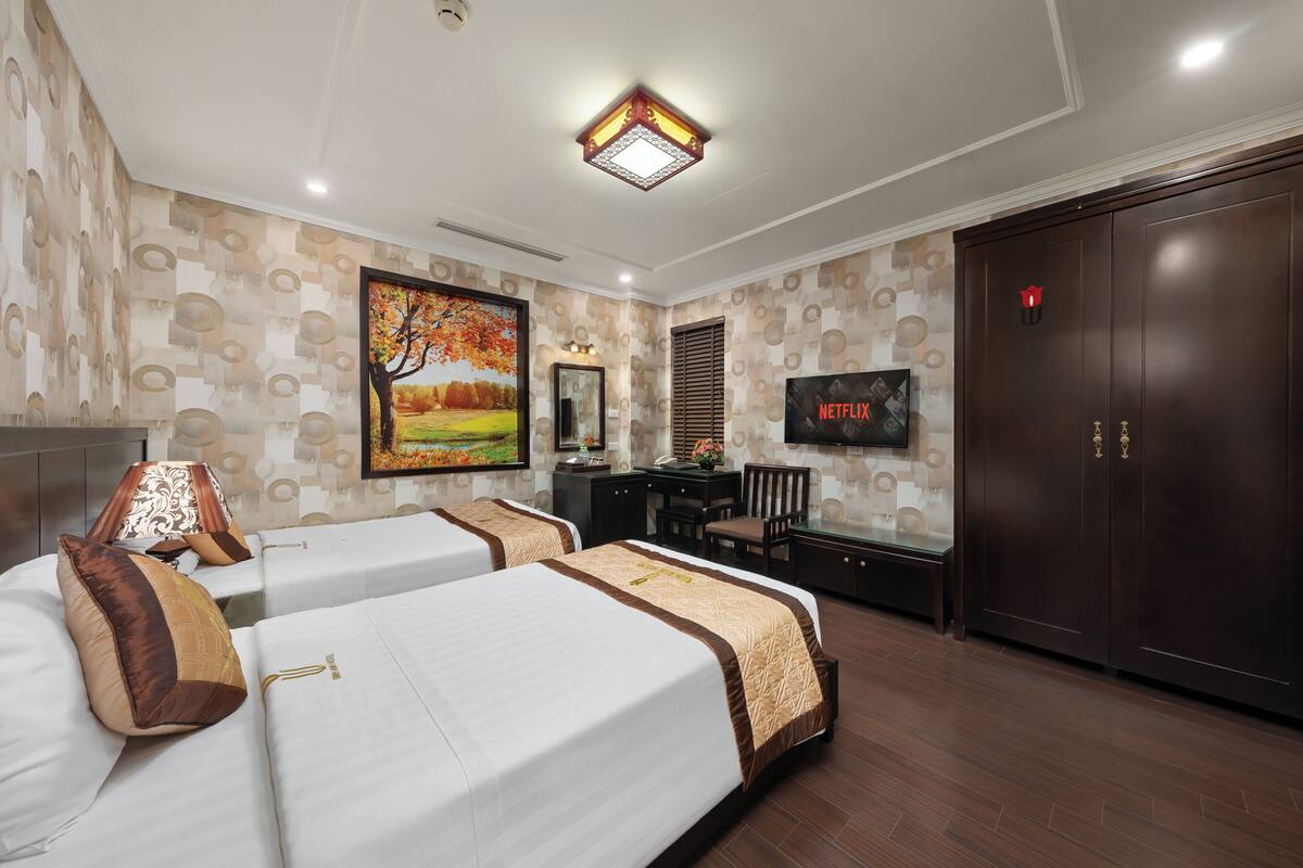 A hotel room with two beds, a desk, a TV, and a wardrobe.