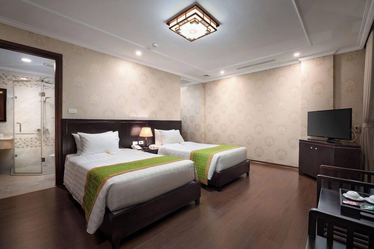 A hotel room with two beds, a TV, a desk, and a shower area.