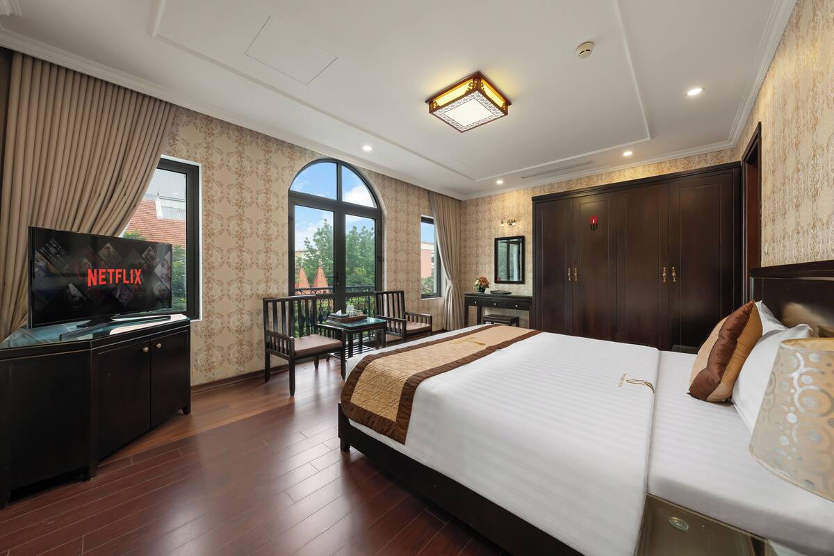A hotel room with a large bed, a TV displaying Netflix, a desk with a chair, a wardrobe, and a balcony with a view.