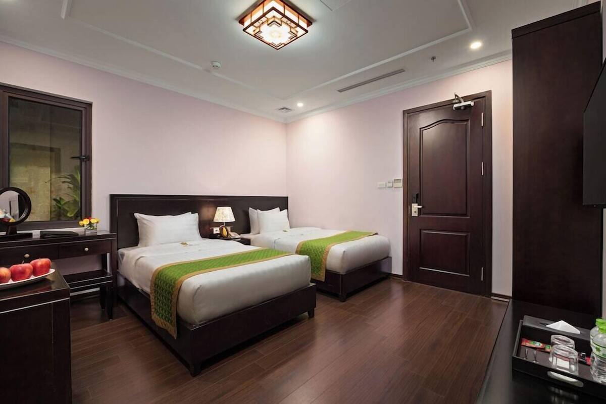 A hotel room with two beds, a desk with a lamp, a dresser, and a television.