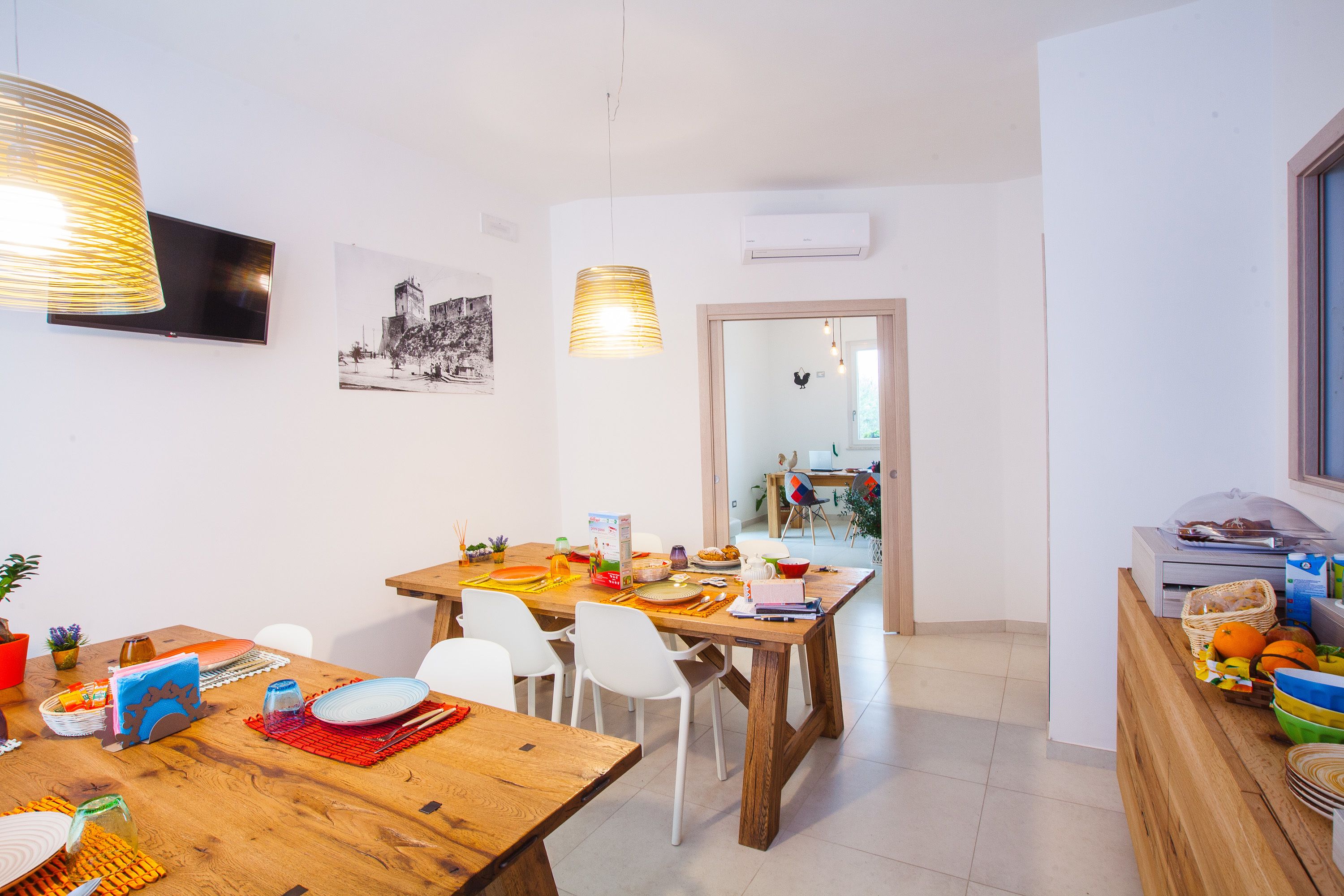 A dining area with a wooden table, white chairs, and a television mounted on the wall.