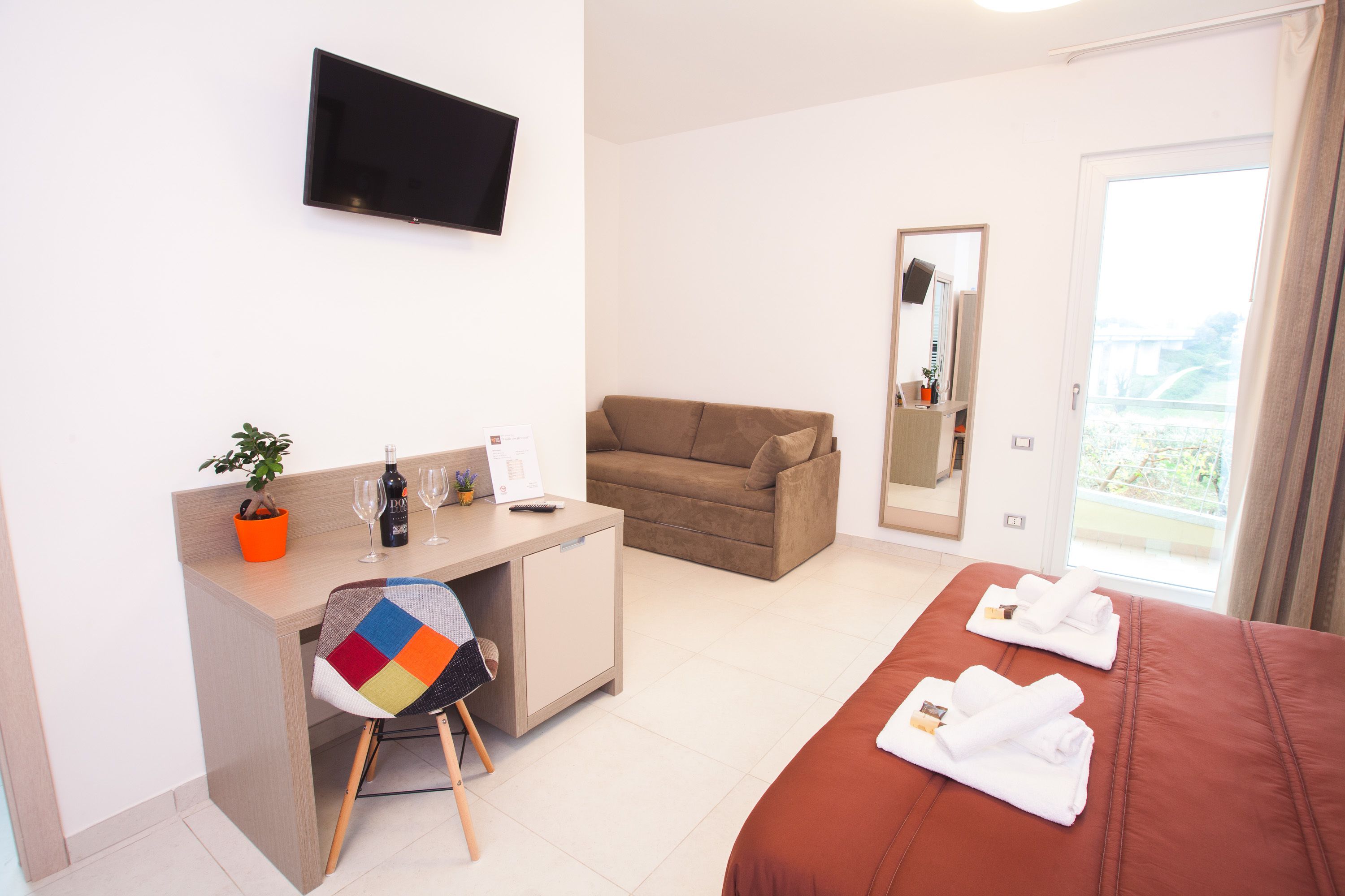Ein Hotelzimmer mit Bett, Schreibtisch mit Stuhl, Fernseher, Sofa und Balkon mit Blick.