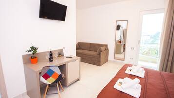 Ein Hotelzimmer mit Bett, Schreibtisch mit Stuhl, Fernseher, Sofa und Balkon mit Blick.