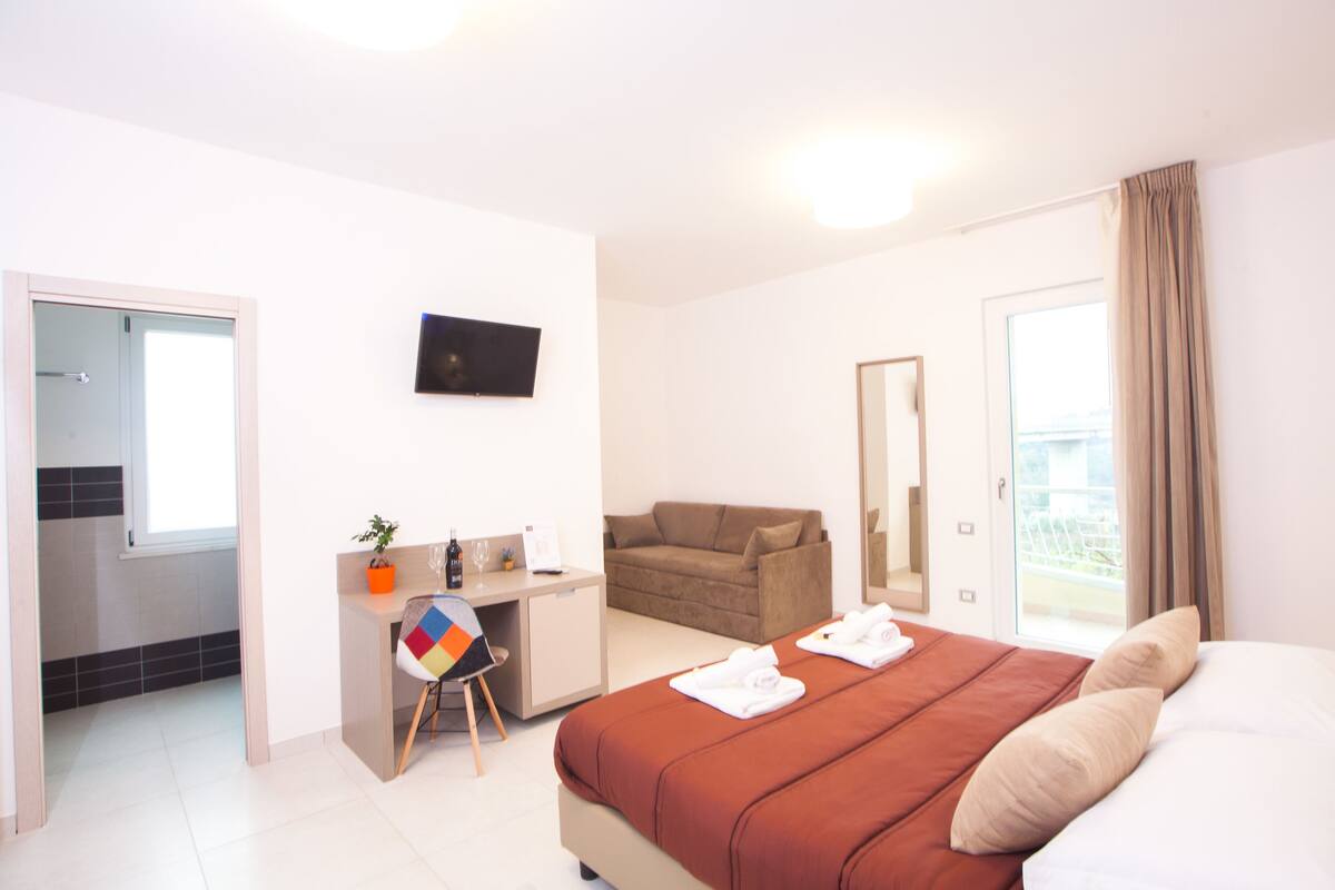 Une chambre d’hôtel avec un lit, un bureau, une chaise, une télévision et un balcon.