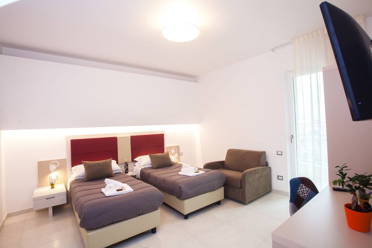 Une chambre d’hôtel avec deux lits, un canapé, une télévision et une plante en pot.
