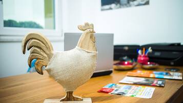 Eine Holz-Hahn-Skulptur steht auf einem Holztisch, im Hintergrund befinden sich ein Laptop und einige Broschüren.