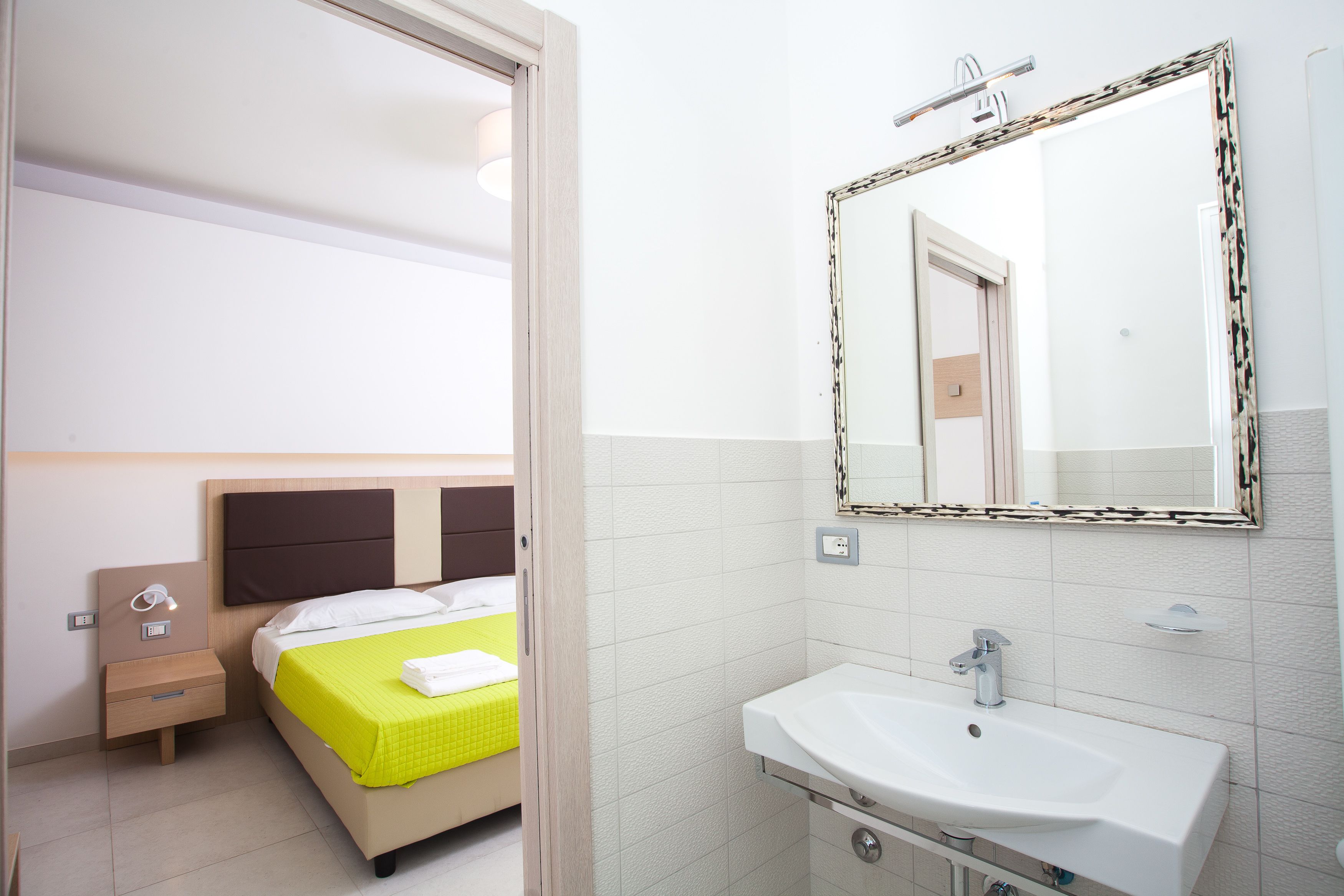 A hotel room with a bed, bedside table, and a bathroom with a sink and mirror.