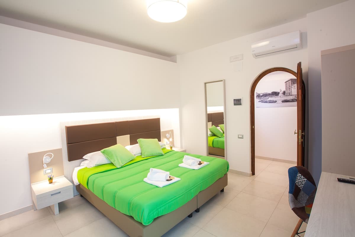 Une chambre moderne avec un grand lit, une literie verte, une table de chevet avec une lampe et une chaise.