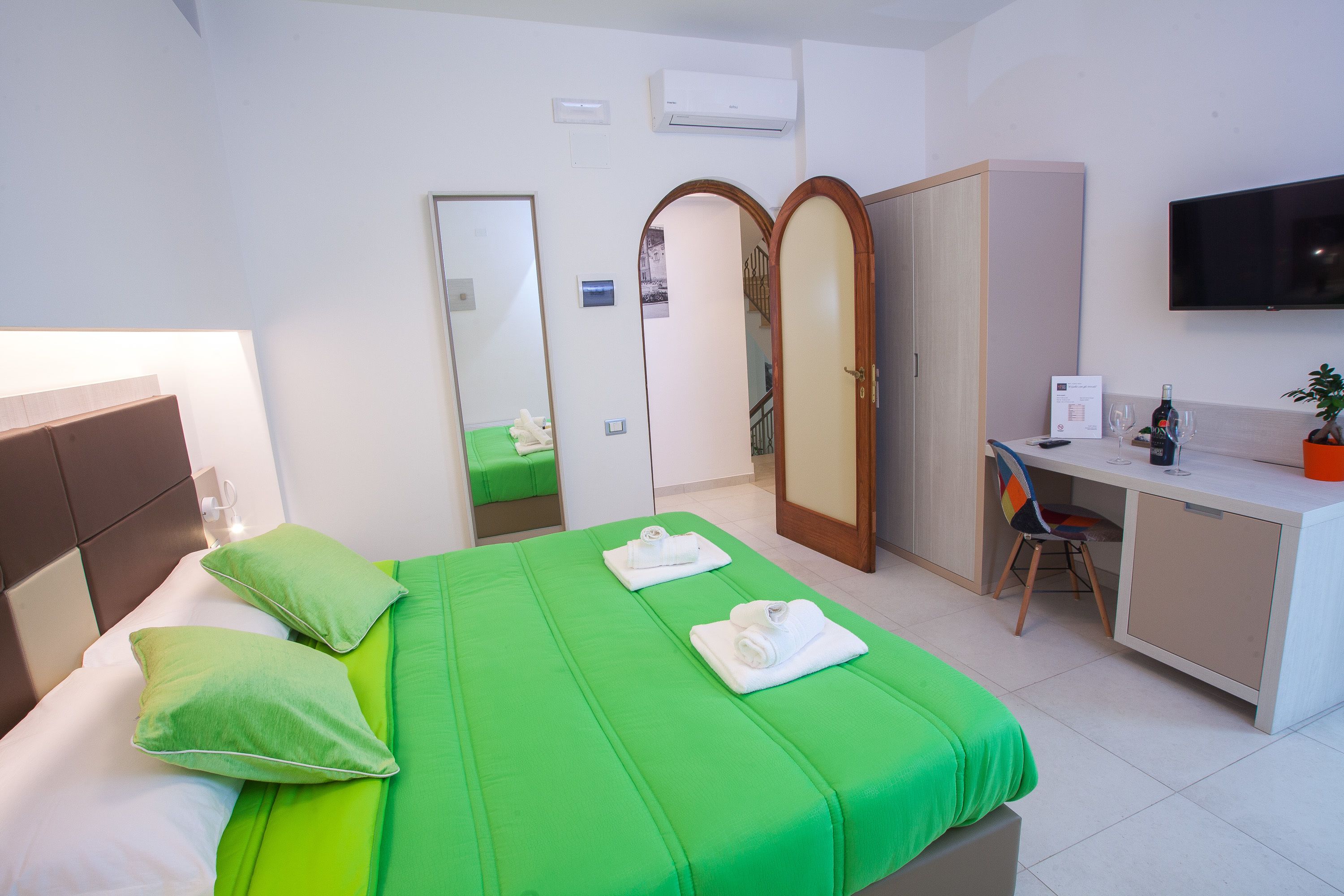 Habitació d'hotel amb un llit, roba de llit verda, escriptori amb cadira, televisió i armari.