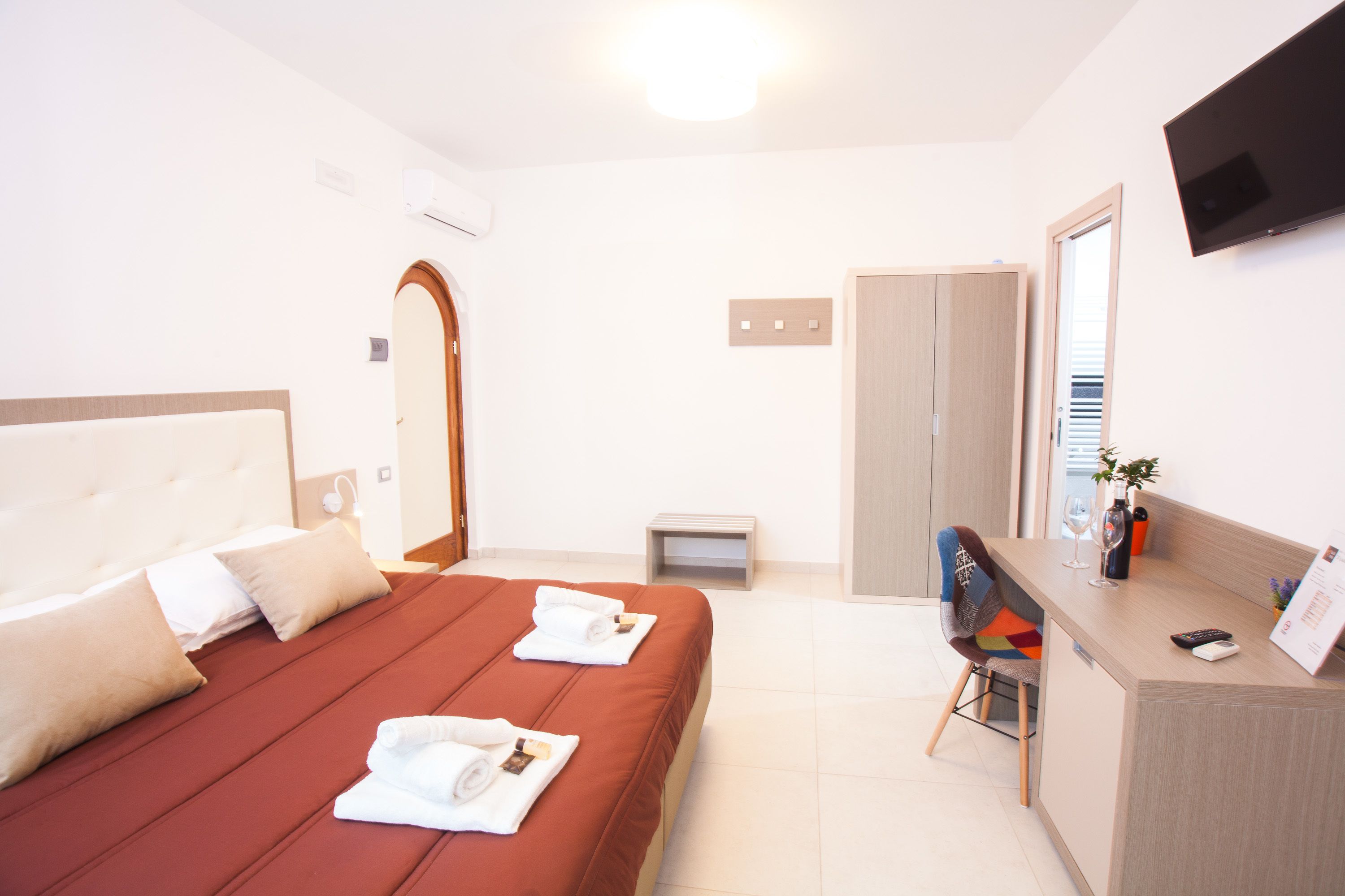 Una camera d'albergo con un letto, una scrivania, una sedia, una TV e un armadio.