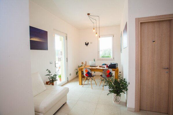 Una sala moderna con un sofá blanco, una mesa de comedor de madera con sillas, una computadora portátil y una lámpara colgante.