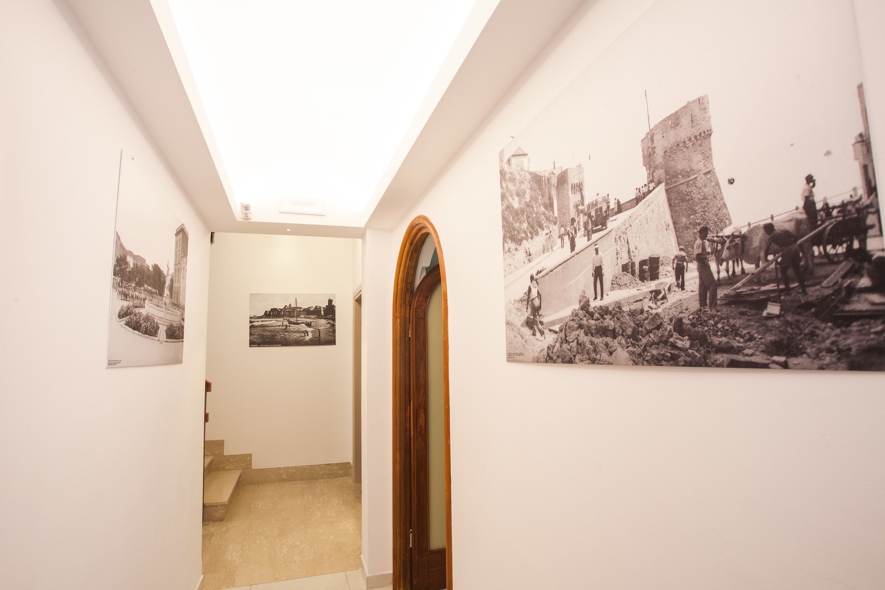 Un pasillo con fotografías en blanco y negro en las paredes, una puerta de madera y una escalera que conduce a otra habitación.