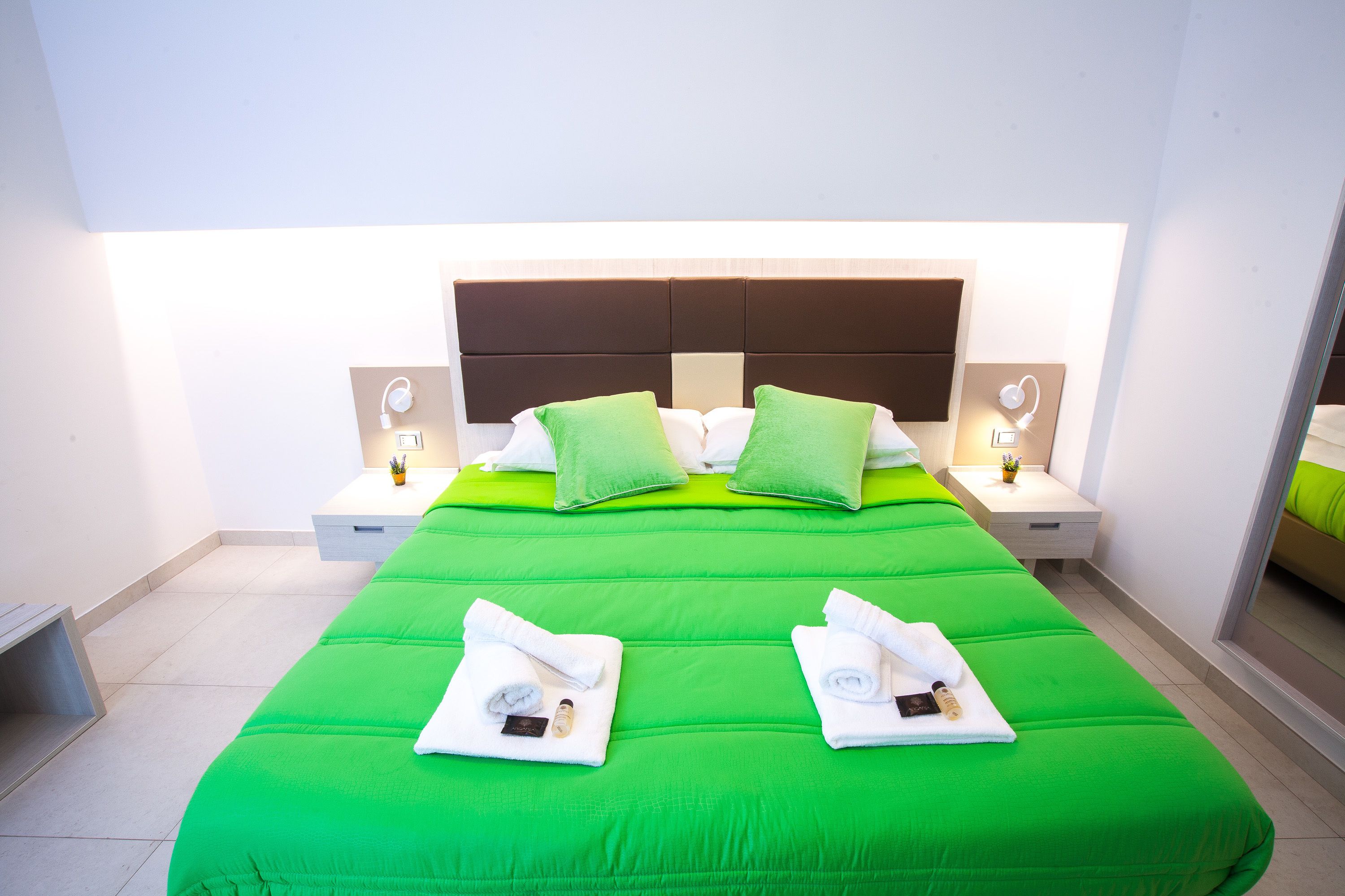 A hotel room with a large bed, green bedding, two nightstands with lamps, and a headboard.