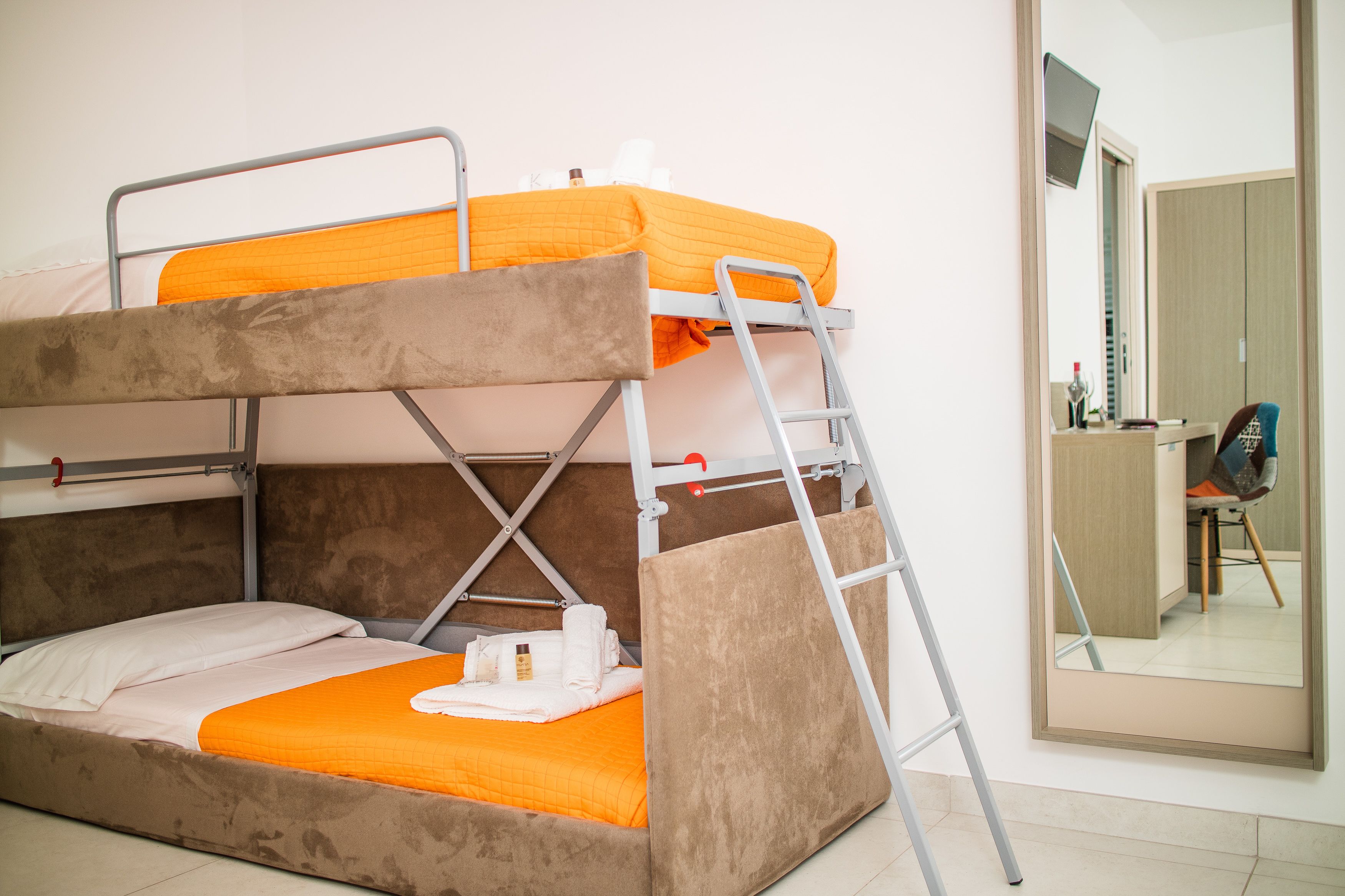Una cama litera con una manta naranja, una escalera y una mesita con una botella y una taza.