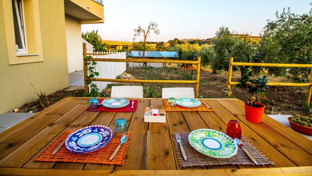 An outdoor dining table set with plates, cutlery, and glasses, surrounded by chairs and a wooden fence. - Il Gallo con gli Stivali (Termoli)