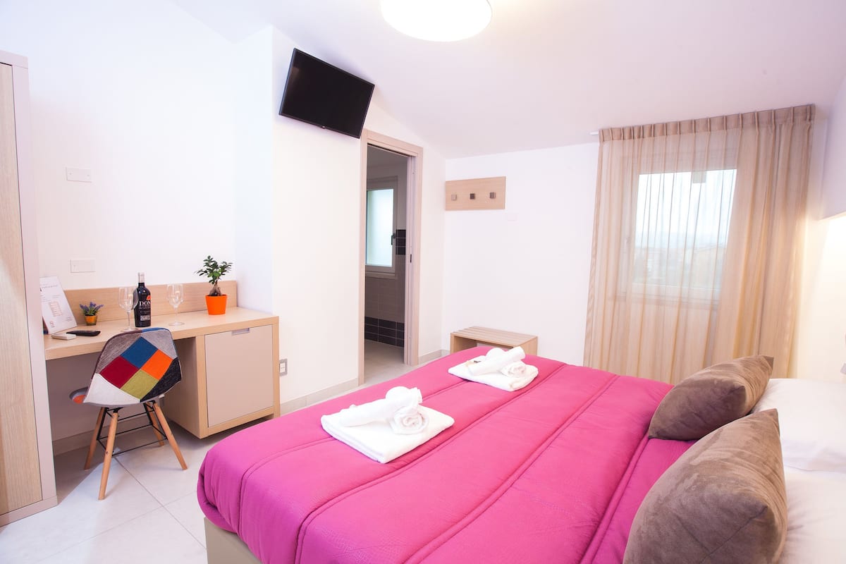 Une chambre d’hôtel avec un lit, un bureau, une chaise, une télévision et une fenêtre avec des rideaux.