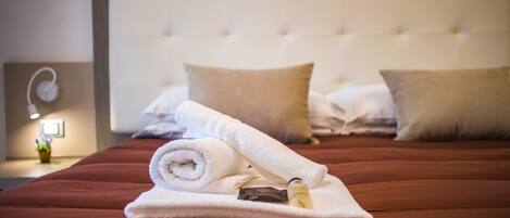 A neatly made bed with a rolled white towel and a bottle on it, a white headboard, and two pillows.