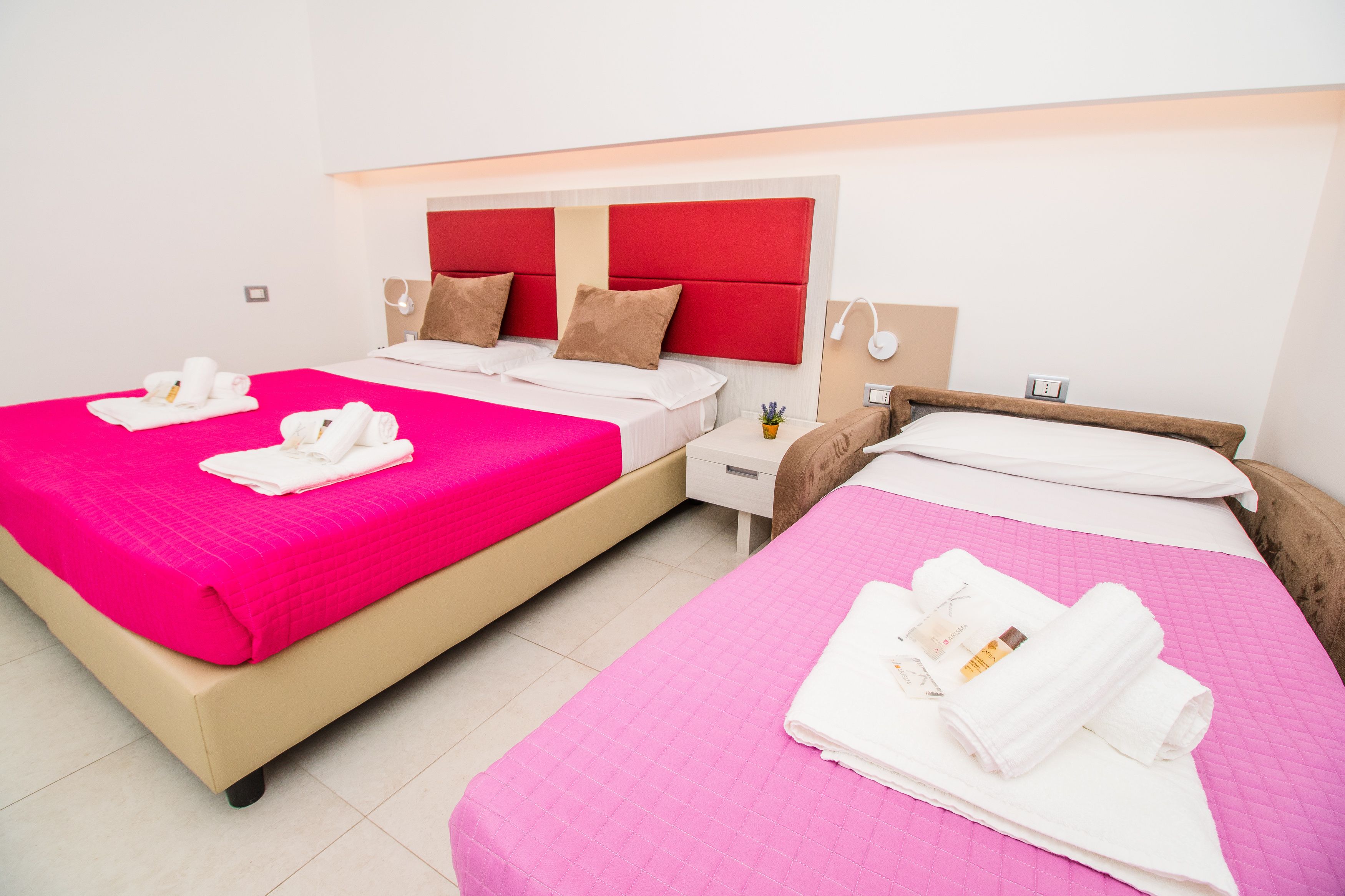 Habitación de hotel con dos camas, cada una con una colcha rosa y toallas blancas.