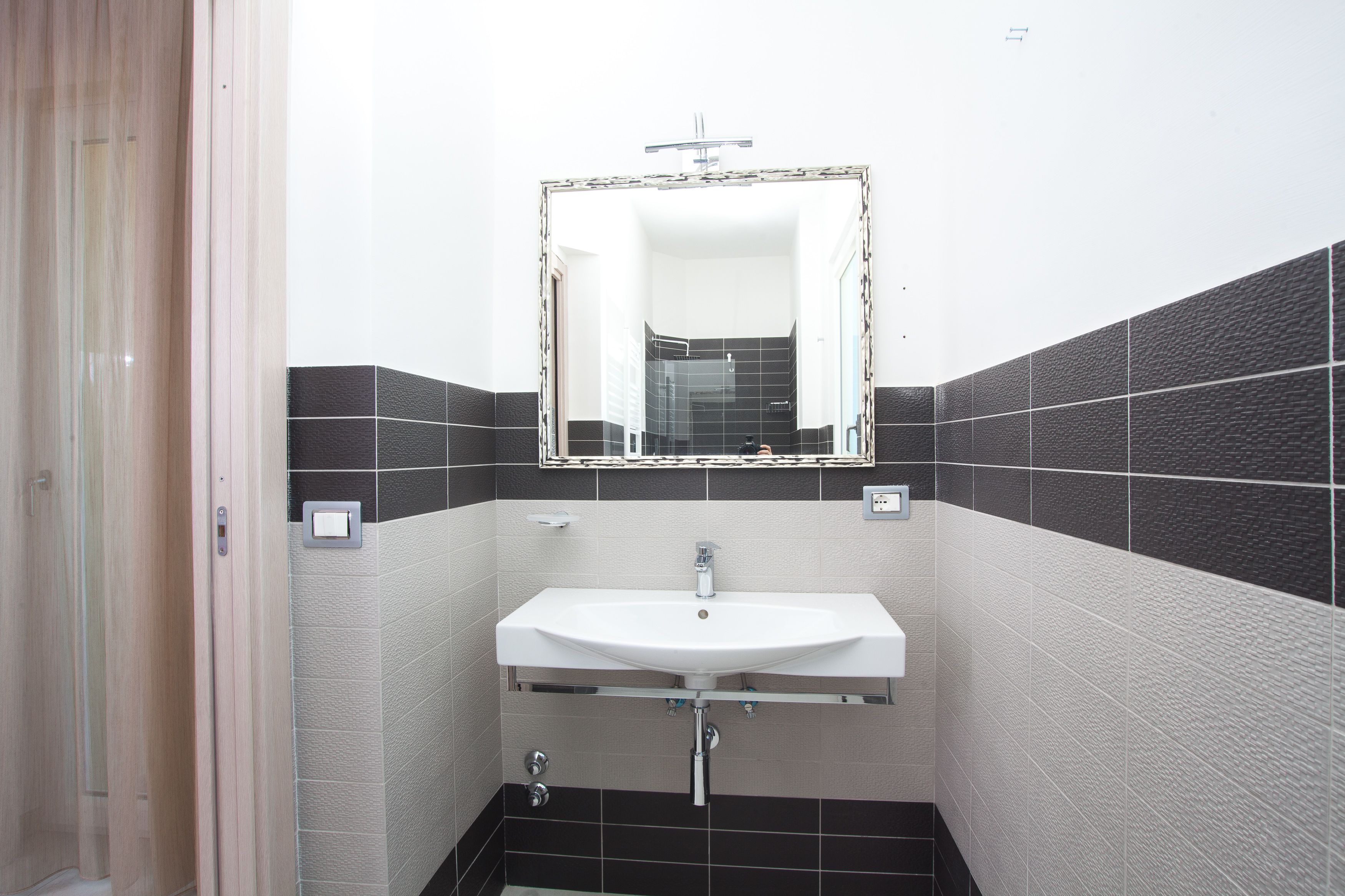 A bathroom with a white sink, a mirror, and black and white tiled walls.