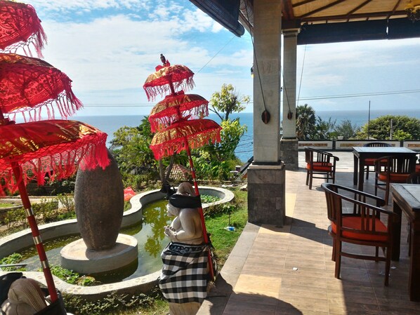 Un espacio al aire libre techado con sombrillas rojas, una estatua y vista al mar.