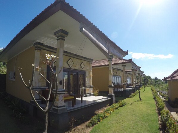 A traditional building with a tiled roof, a porch with a bench, and a well-maintained lawn. - Bali Bhuana Villas (Karangasem)