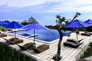 Een buitenzwembad, een infinitypool en ligstoelen