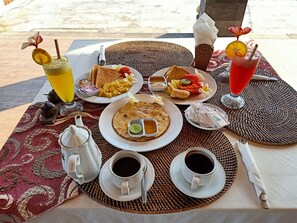Un desayuno con platos de comida, tazas de café y una bebida sobre un tapete tejido.