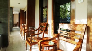 Un pasillo con sillas y mesas de madera, ventanas amplias y vistas al verdor exterior.