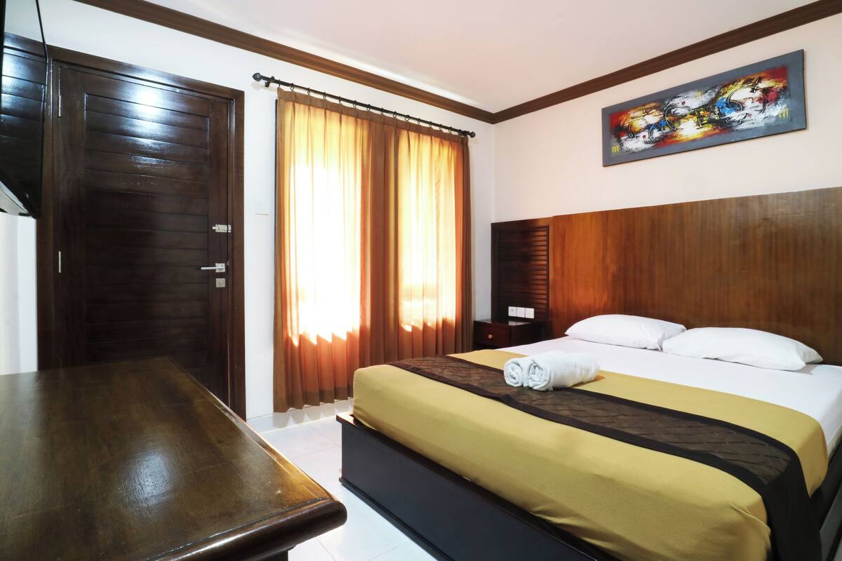 A hotel room with a wooden bed, a desk, and a large window with curtains.
