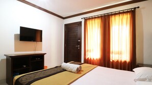 Una habitación de hotel con cama, televisión montada en la pared, escritorio y silla, y una puerta.