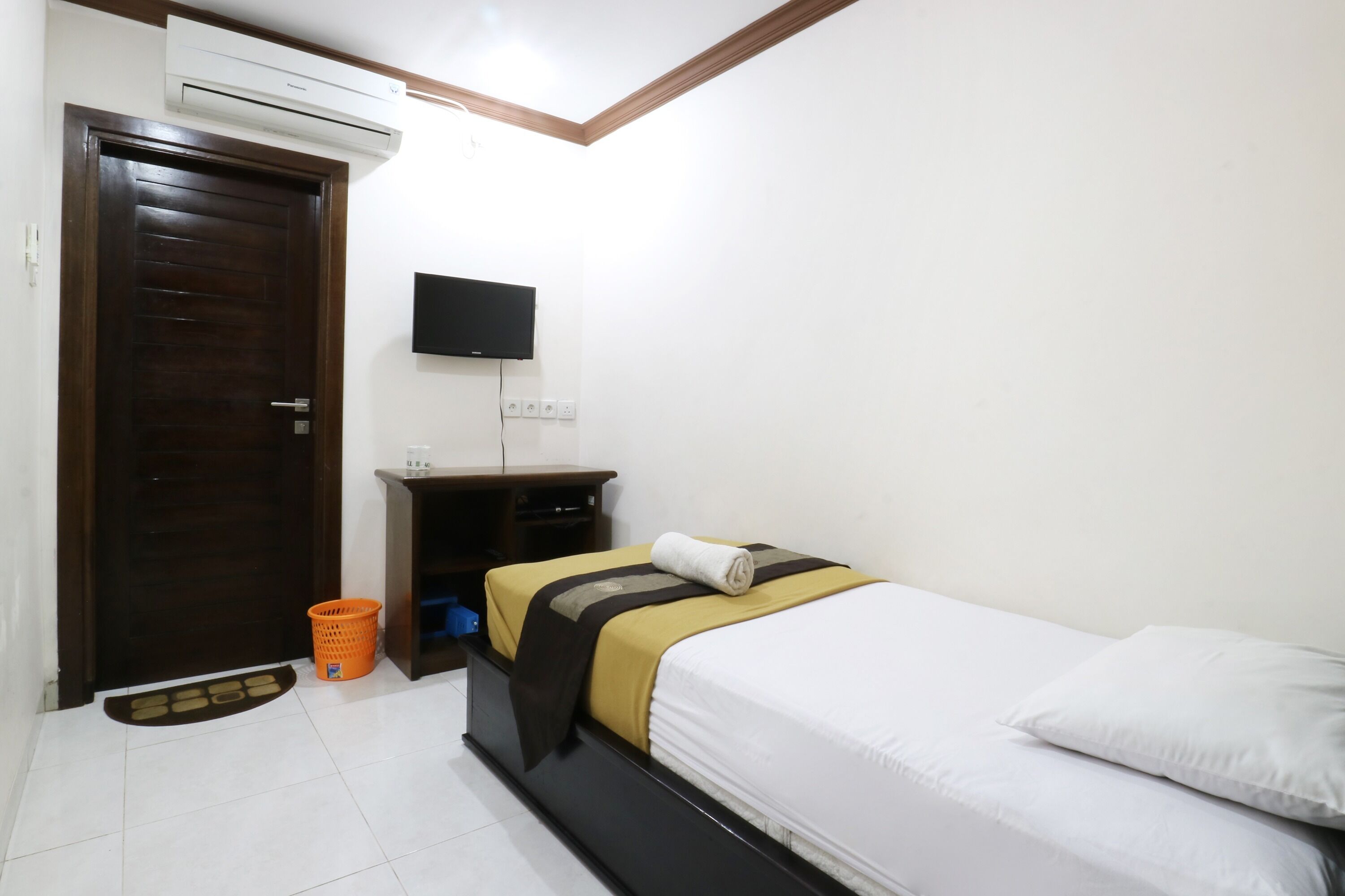 Habitación de hotel con una cama, un televisor montado en la pared, una puerta de madera y un equipo de aire acondicionado.