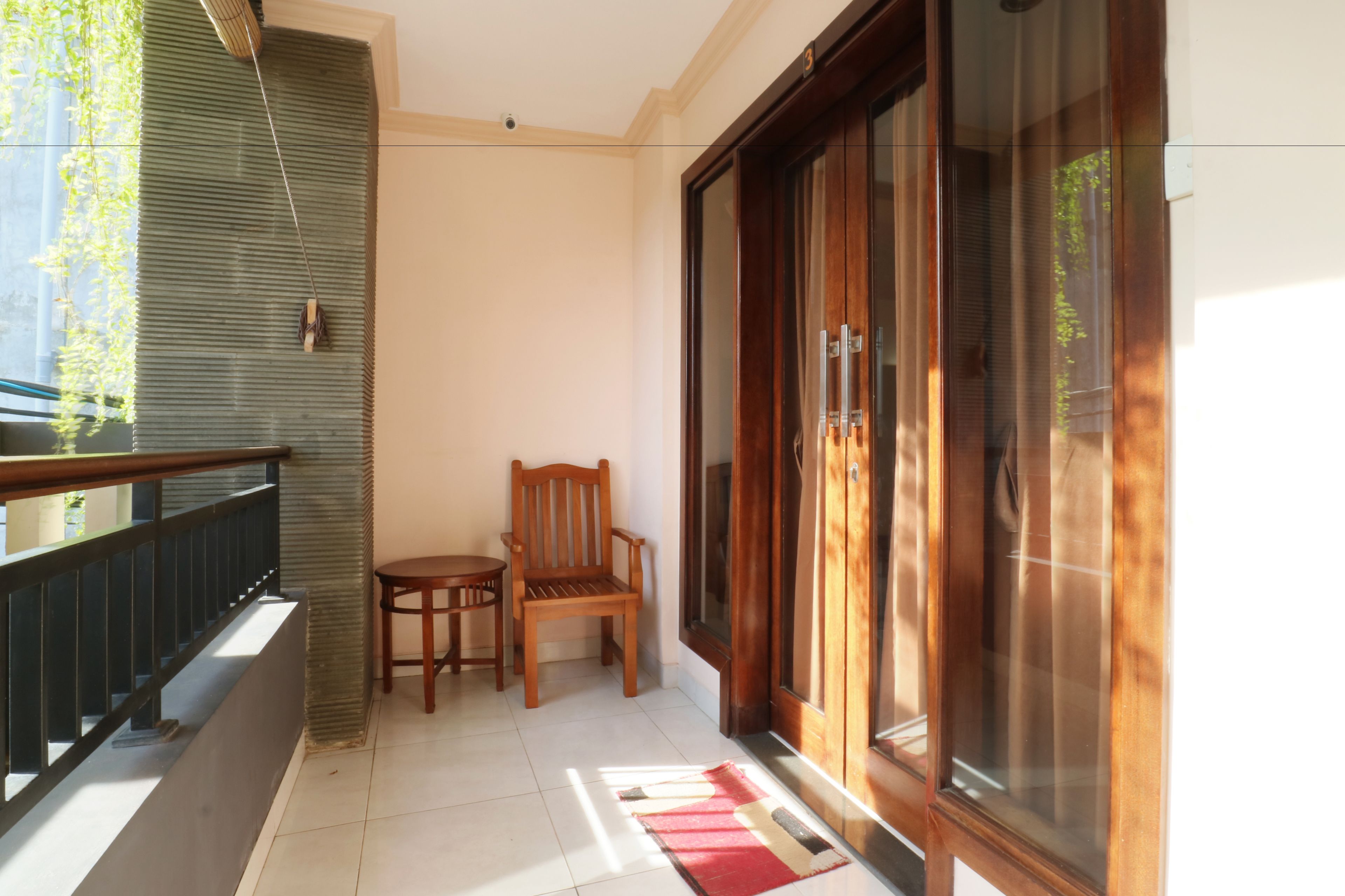 Ein Balkon mit einem Holzstuhl, einem kleinen Tisch und einer roten Teppich.