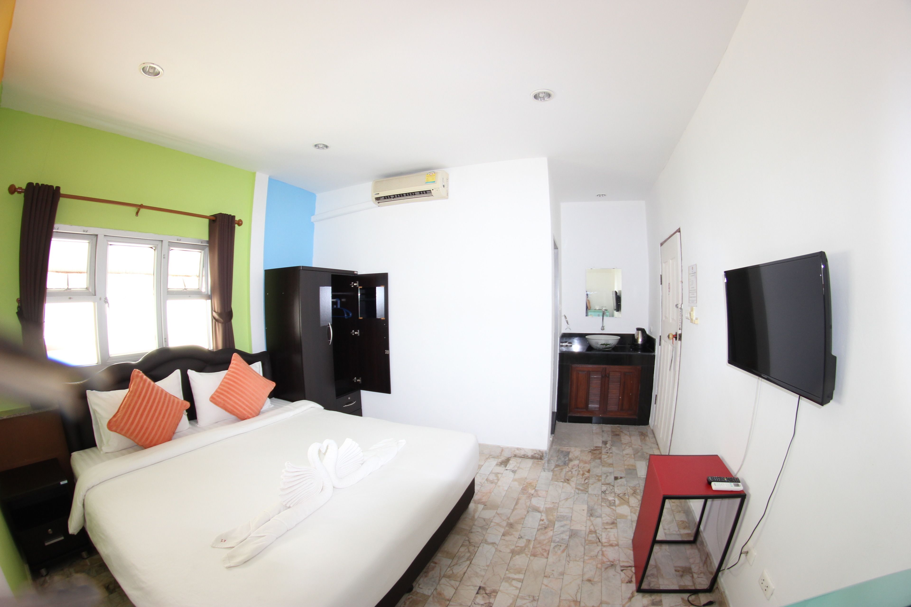 Quarto de hotel com uma cama, televisão, escrivaninha, guarda-roupa e casa de banho visível através de uma porta aberta.