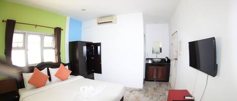 Quarto de hotel com uma cama, televisão, escrivaninha, guarda-roupa e casa de banho visível através de uma porta aberta.